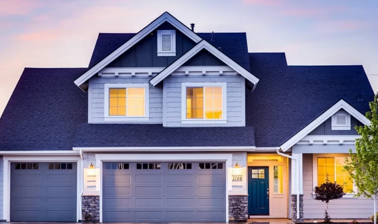 Modern suburban house with a double garage, large windows, and illuminated interiors at dusk